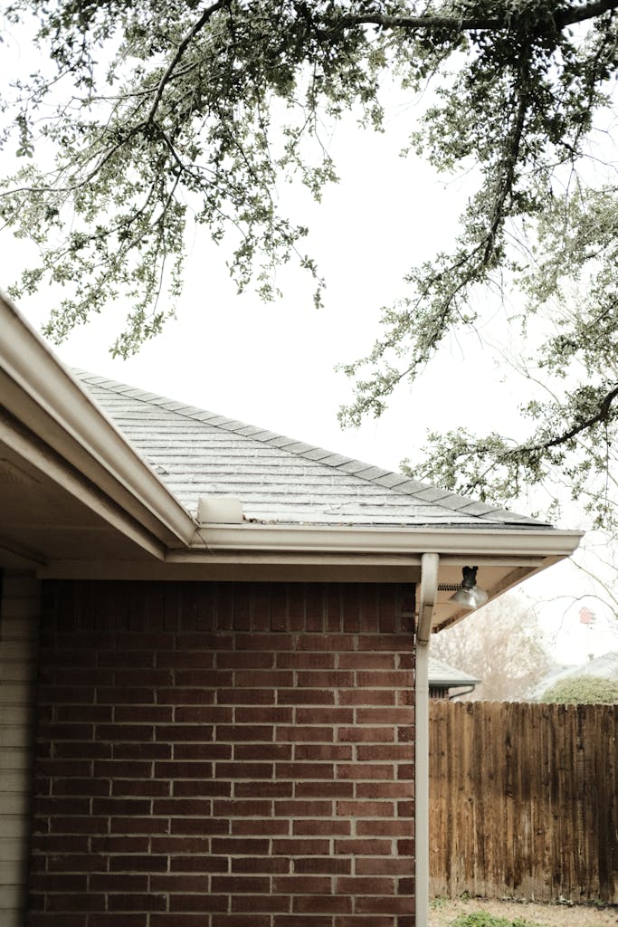 A serene view of a red brick house corner with overhanging tree branches.